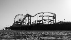 Black and white photo of Santa Monica Pier with its roller coaster and Ferris wheel above the waves