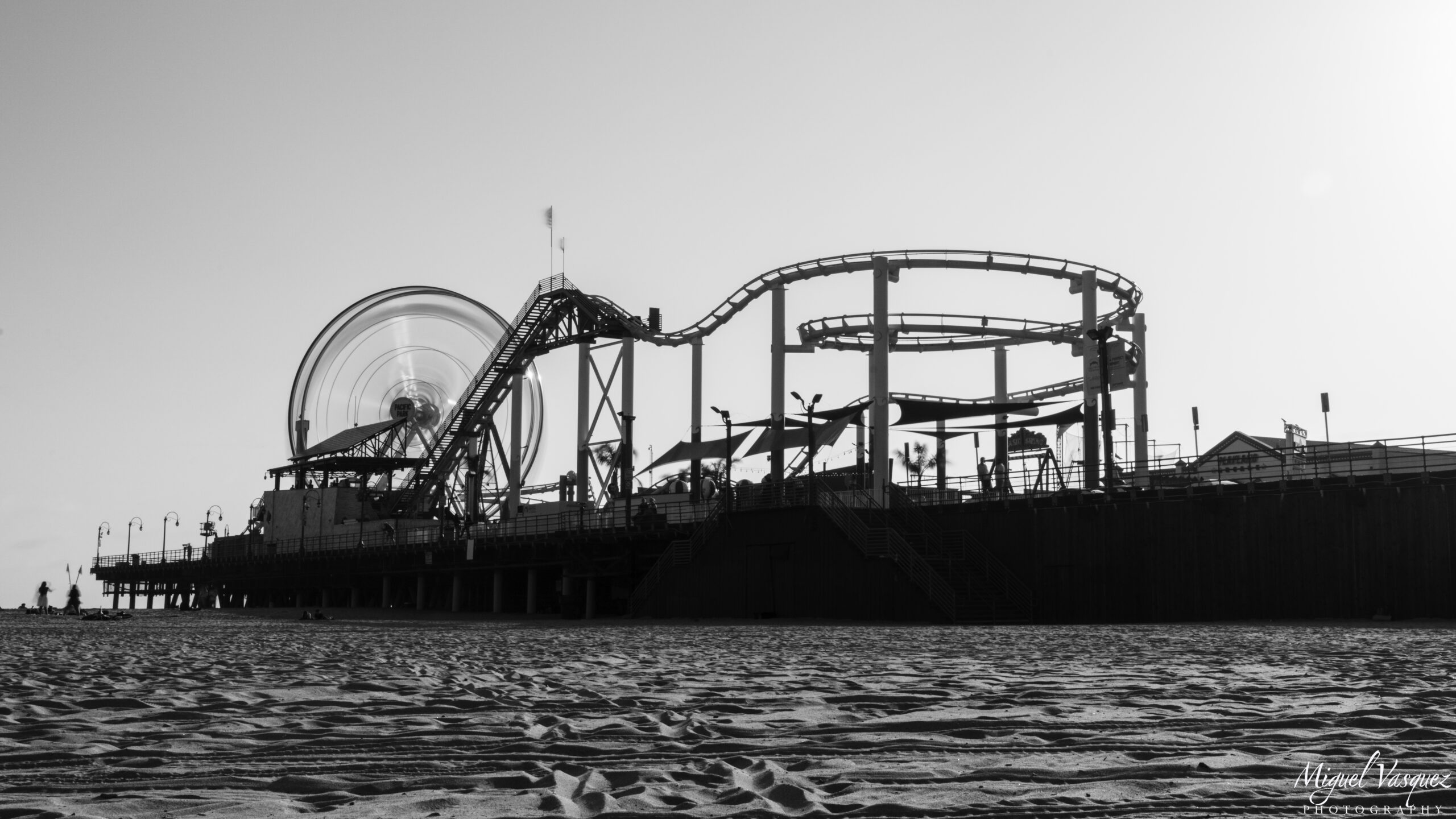 Black and white photo of Santa Monica Pier with its roller coaster and Ferris wheel above the waves